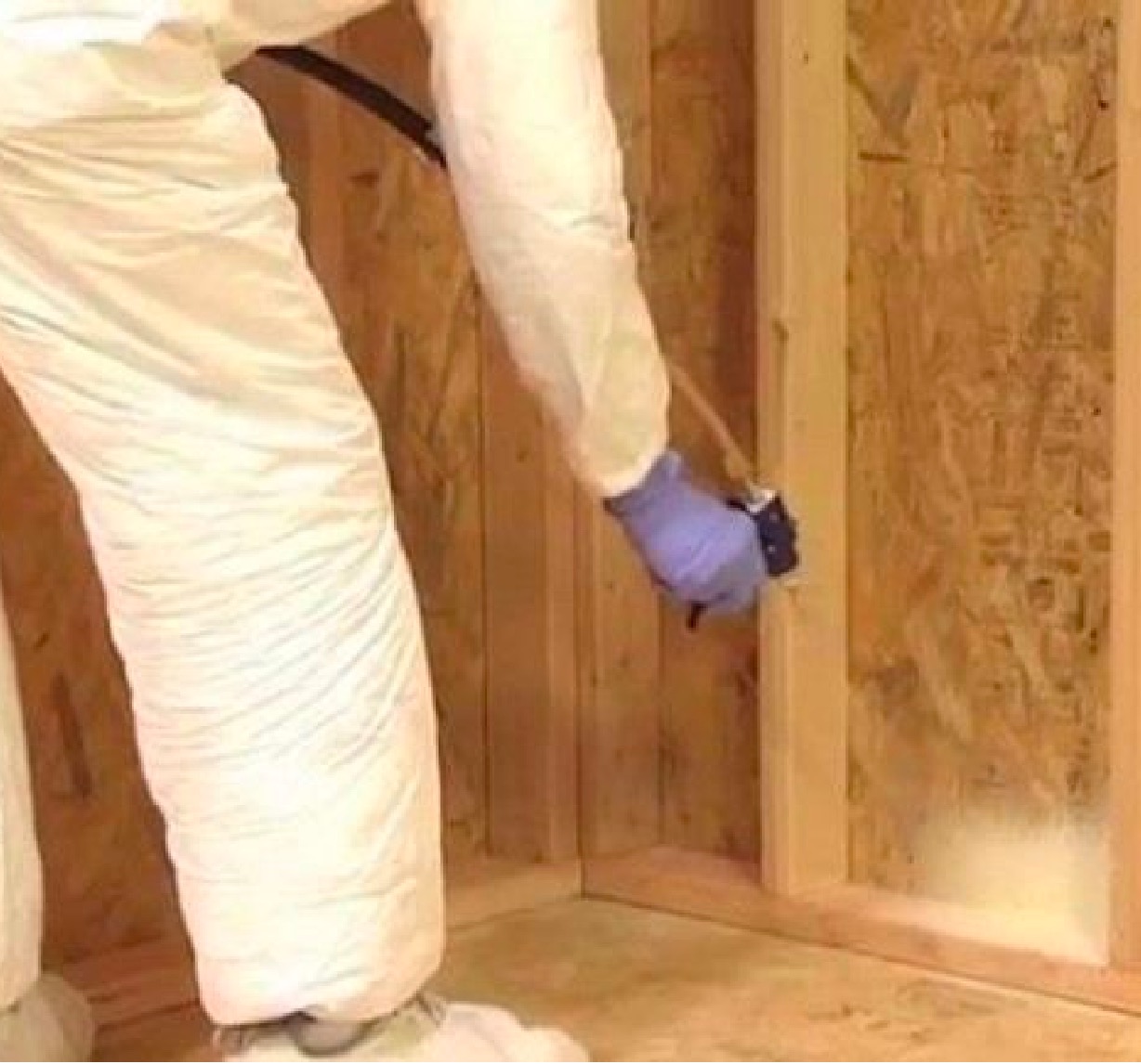 Worker in white protective clothing spraying insulation into a wall